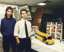 Photograph of Industrial Design programs stand next to a model of their design