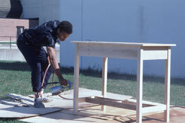 Photograph of a student applying sealant to piece of furniture