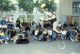 Photograph of a busker riding a unicycle while juggling fire sticks in the Student Centre.