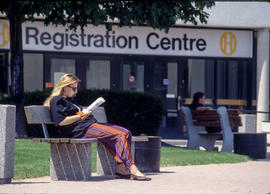 Photograph of students relaxing in the sun on the benches outside the Registration Entrance.