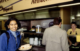Photograph of a student walking away with a meal while another customer examines the food choices