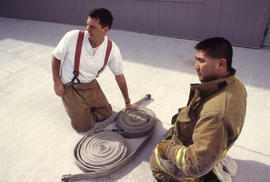 A photograph of two student firefighters and a rolled up firehose at North