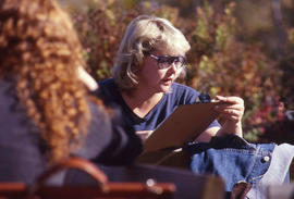 Photograph of an unknown person wearing glasses and seated outside with others